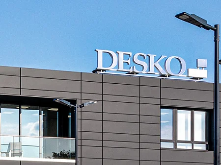 Moderno edificio de la empresa DESKO con fachada oscura, banderas en primer plano y cielo azul.