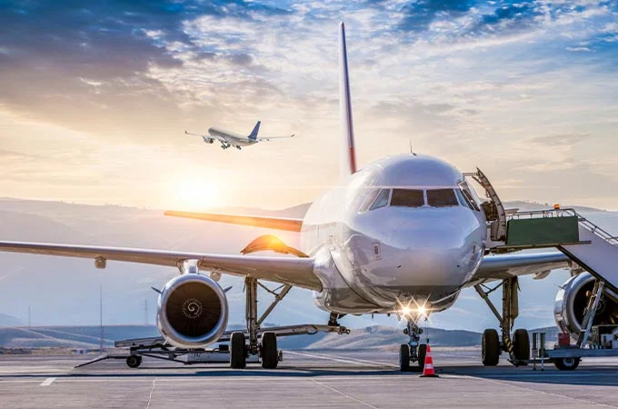 Passagierflugzeug auf dem Vorfeld eines Flughafens, Boarding &uuml;ber Treppe, startendes Flugzeug im Hintergrund bei Sonnenaufgang.