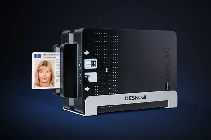 Ein DESKO-Dokumentenscanner liest einen Personalausweis ein, der seitlich eingeschoben ist; das Ausweisfoto ist sichtbar.
