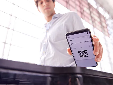 Un homme tient un smartphone avec une carte d'embarquement numérique et un code QR au-dessus d'un terminal d'accès à l'aéroport.