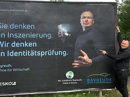 DESKO Mitarbeiter Wojciech Bujak steht vor einer Plakatwand, die ihn mit einem DESKO Scanner in der Hand zeigt.