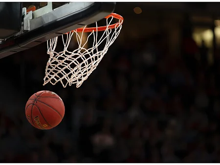 Basketball fliegt durch den Korb und spannt das Netz, während im Hintergrund eine dunkle Zuschauermenge zu sehen ist.