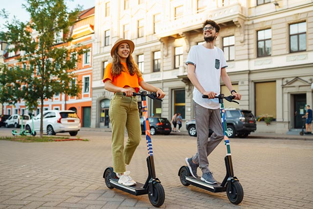 Ein Mann und eine Frau fahren mit E-Scootern durch eine Innenstadt