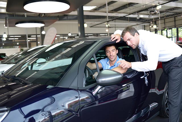Ein Mann sitzt in einem Vorführwagen eines Autohauses und lässt sich vom Verkäufer beraten