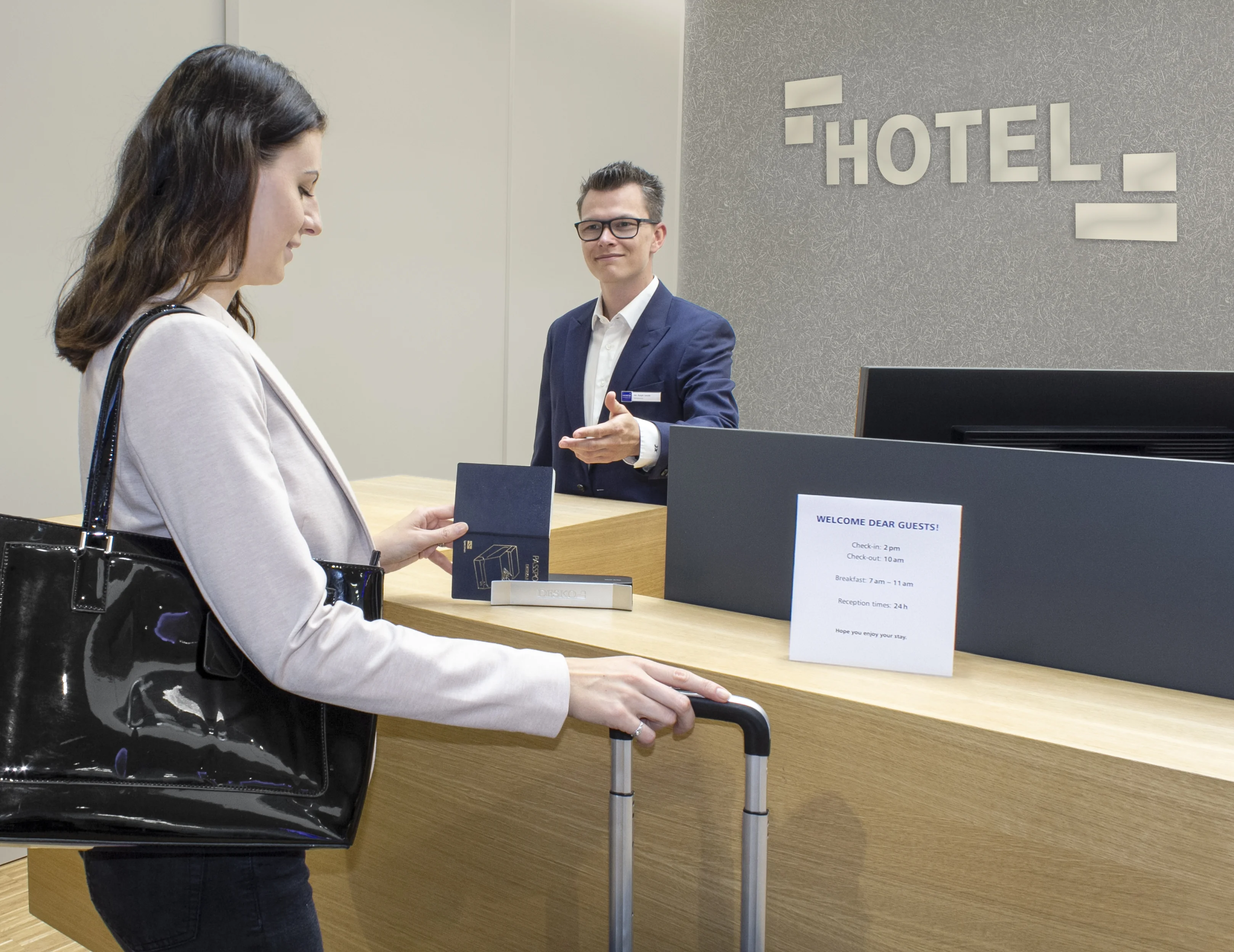 Hotel reception with guest at check-in, handing over an ID card at the counter while the employee takes it.