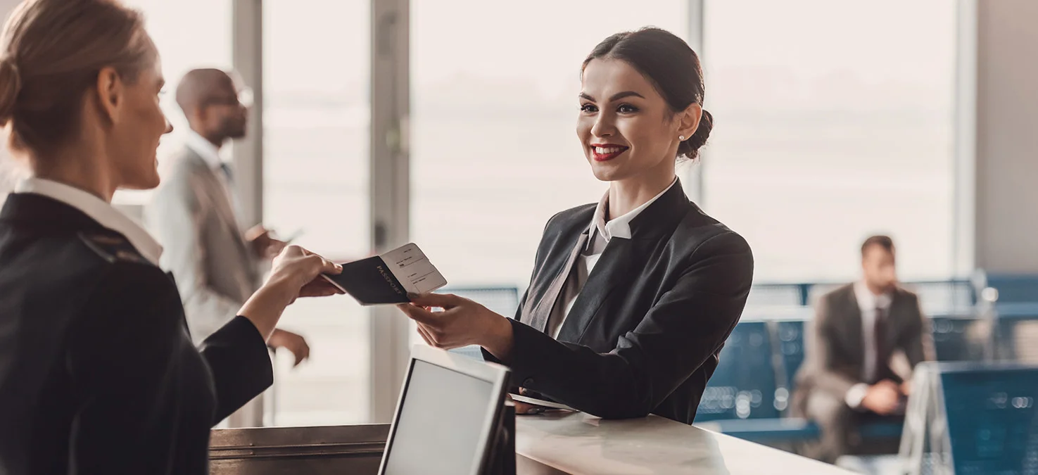 Airport employee collects passport and boarding pass from a passenger at the check-in counter.