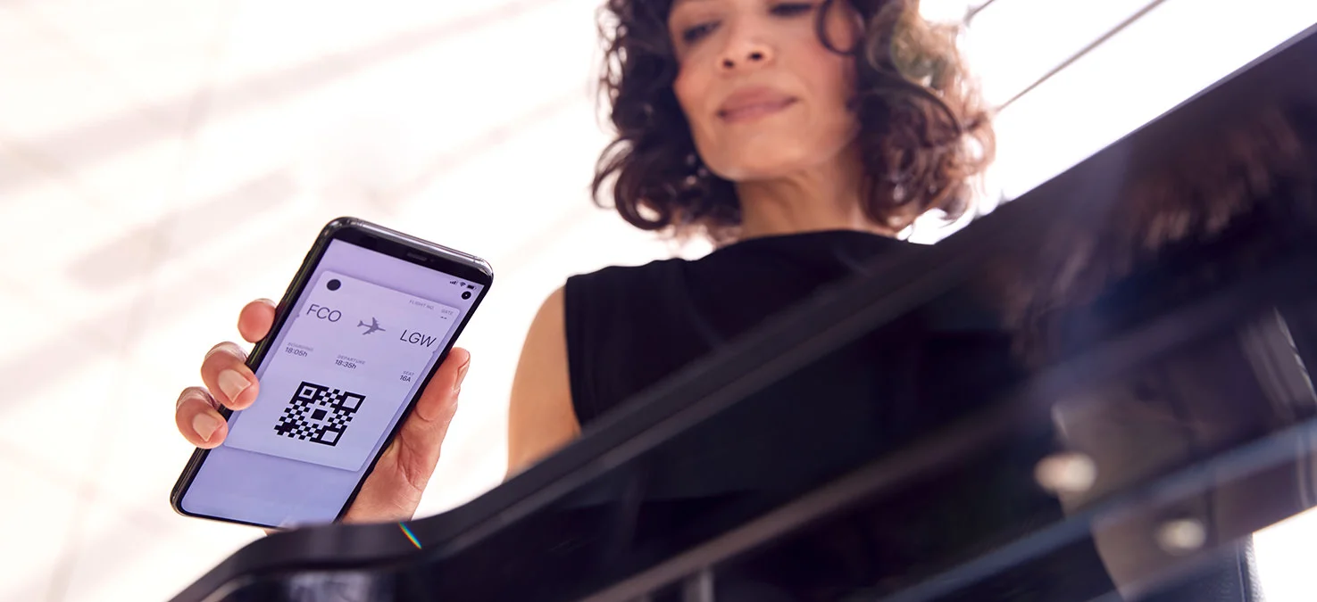 Woman holds a smartphone with a digital boarding pass and QR code in front of a scanner during boarding at the airport.