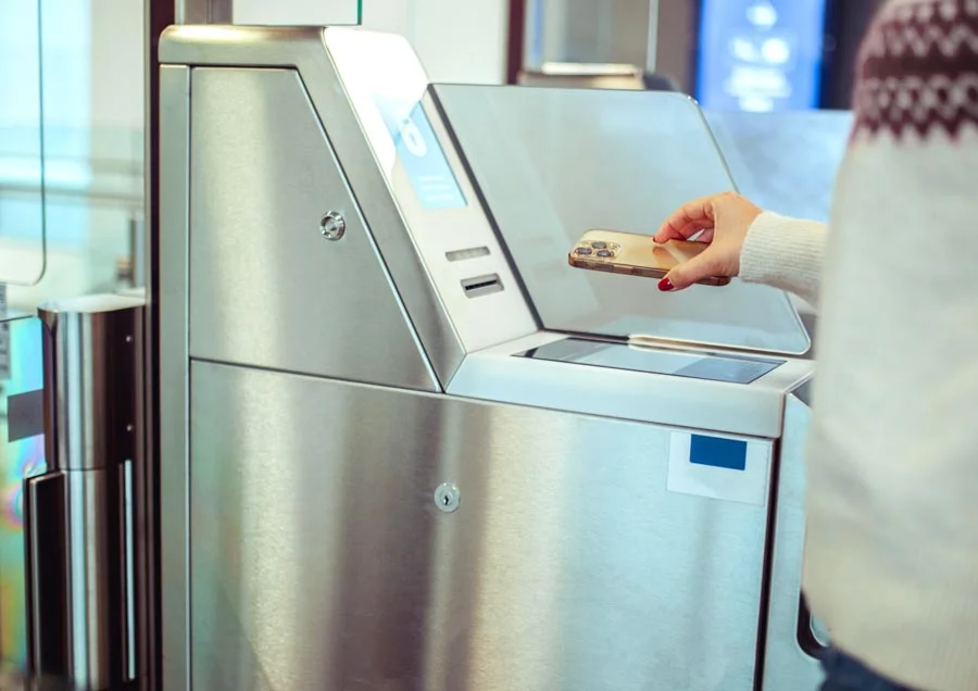 La personne tient son smartphone devant une station de contr&ocirc;le d'acc&egrave;s moderne en acier inoxydable avec &eacute;cran et surface de scannage.