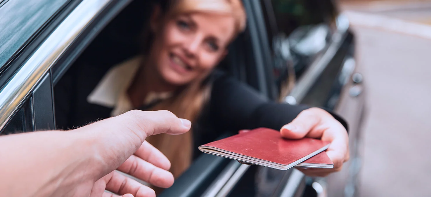 Driver hands two passports out of the open car window to a person checking them on the road.