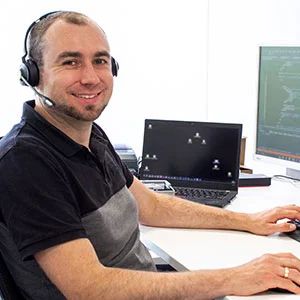 Mann mit Headset sitzt am Schreibtisch vor Laptop und Monitor