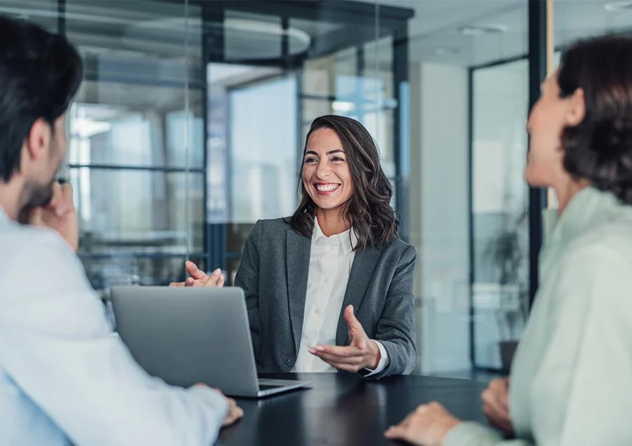 Woman chairing a meeting with laptop at the table and laughing while two colleagues listen in a modern office.