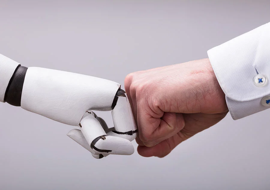 Robot hand and human fist touch for a fist bump in front of a neutral background