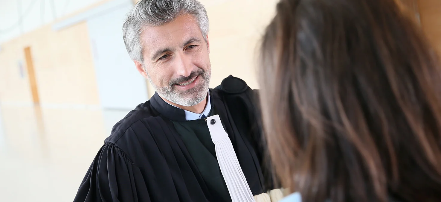 Mann in schwarzer Robe mit wei&szlig;em Beff spricht freundlich mit einer Person, in hellem Flur eines Gerichtsgeb&auml;udes.