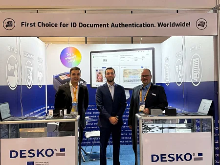 Trois hommes se tiennent sur le stand de DESKO devant des scanners de documents et des moniteurs, avec au-dessus d'eux l'inscription 