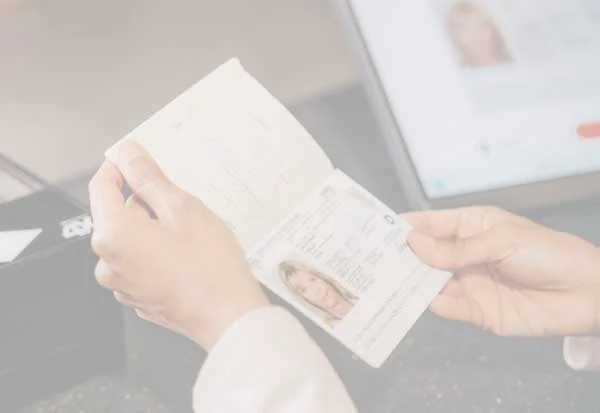 Manos que sostienen un pasaporte abierto con la p&aacute;gina de datos visible, al fondo una pantalla para la verificaci&oacute;n digital de la identidad.