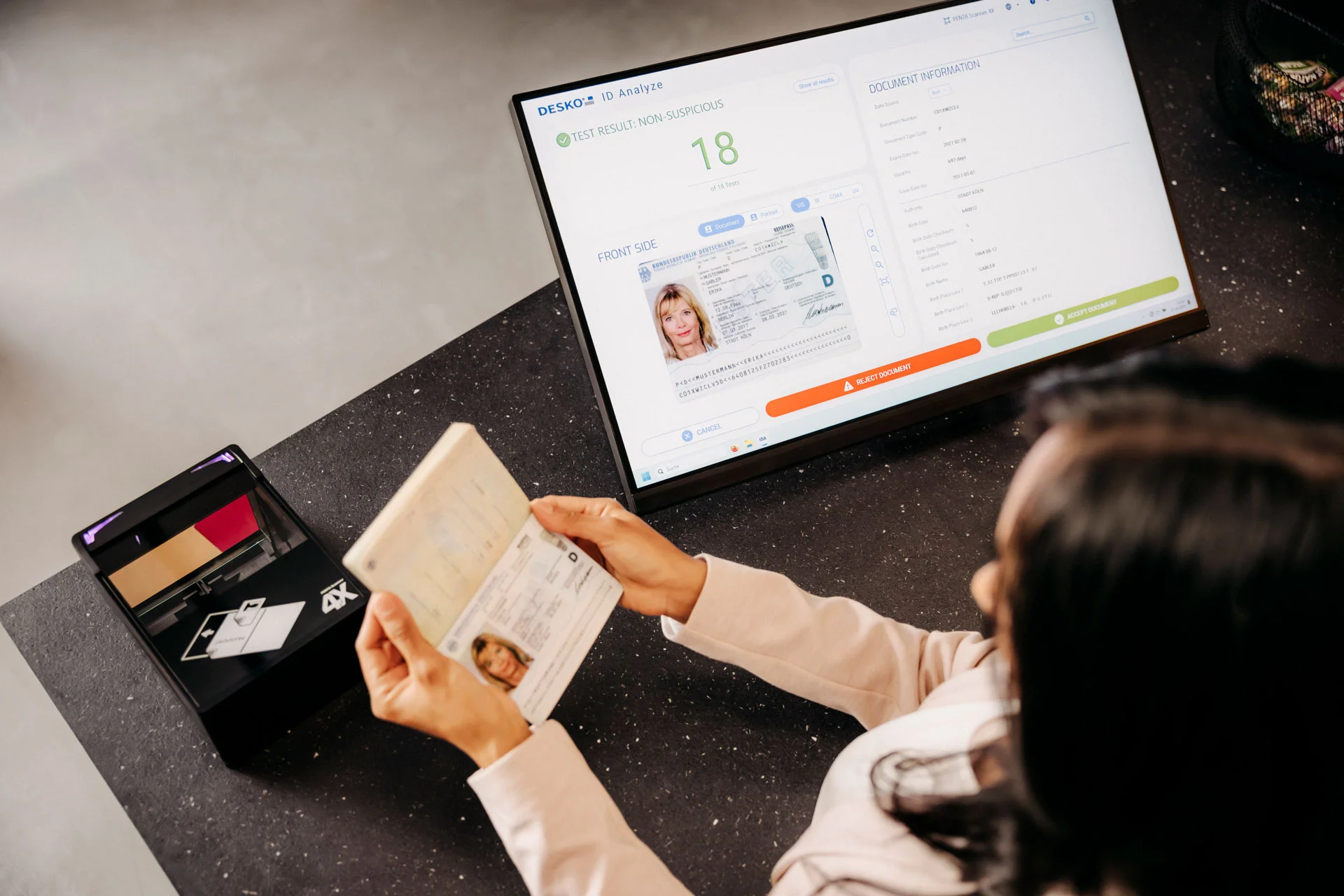Person h&auml;lt einen ge&ouml;ffneten Reisepass vor ein Pr&uuml;fger&auml;t, w&auml;hrend auf einem Bildschirm die digitale Ausweisanalyse mit Pr&uuml;fergebnis angezeigt wird.