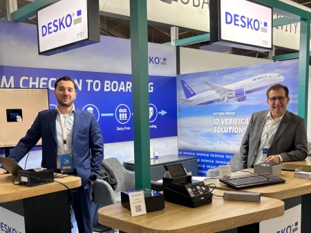 Deux collaborateurs de DESKO se tiennent devant le stand du salon Global Airports Forum à Riyad et regardent la caméra.