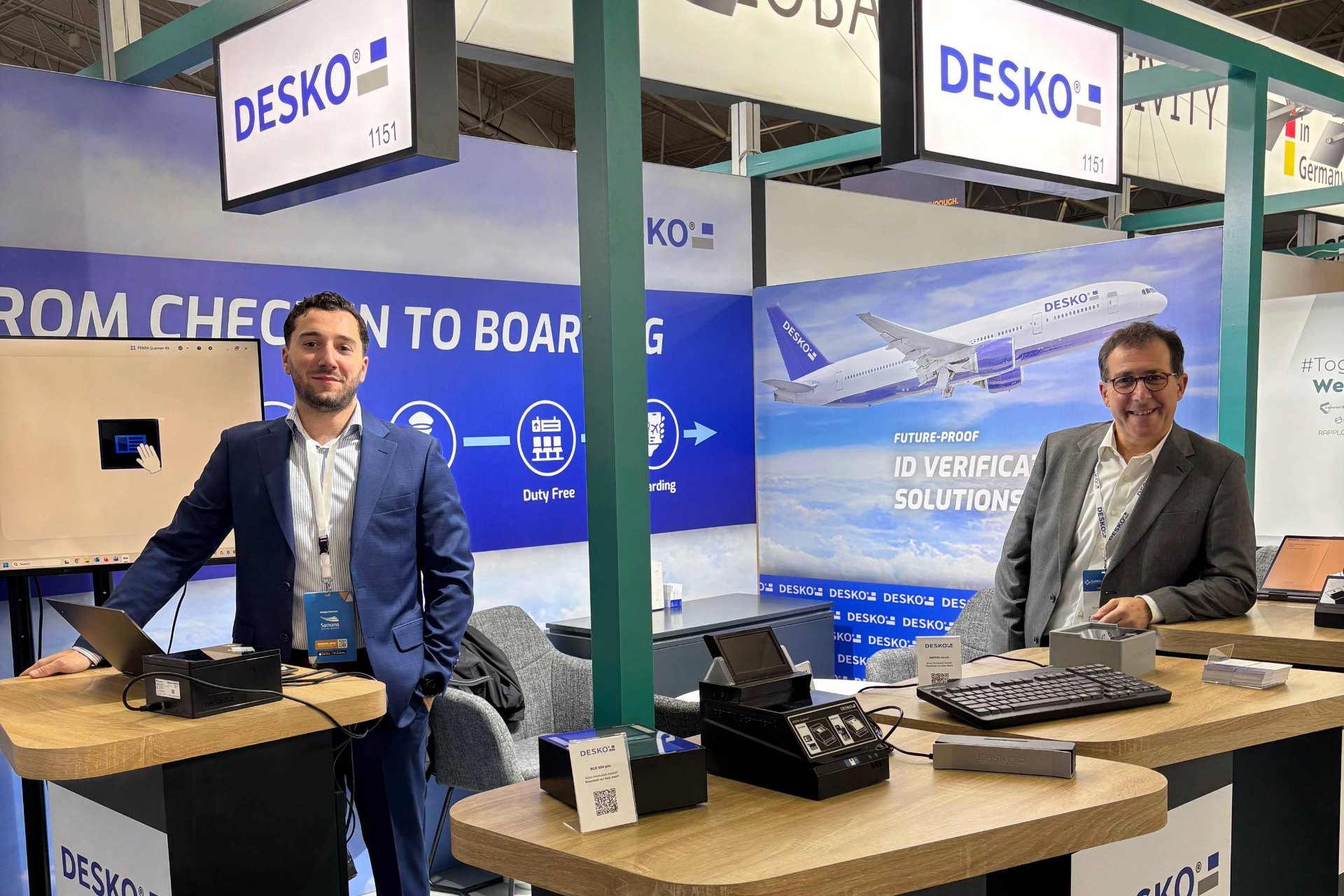 Zwei DESKO Mitarbeiter stehen am Messestand auf der Global Airports Forum in Riyadh und blicken in die Kamera.