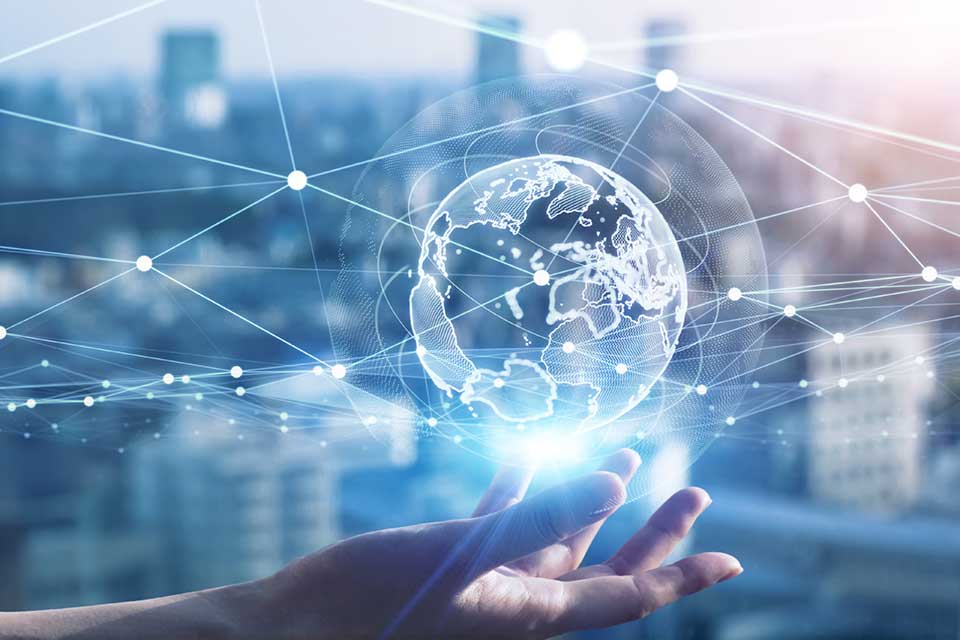 Hand hält eine leuchtende, digitale Weltkugel mit vernetzten Linien vor unscharfer Stadtkulisse.