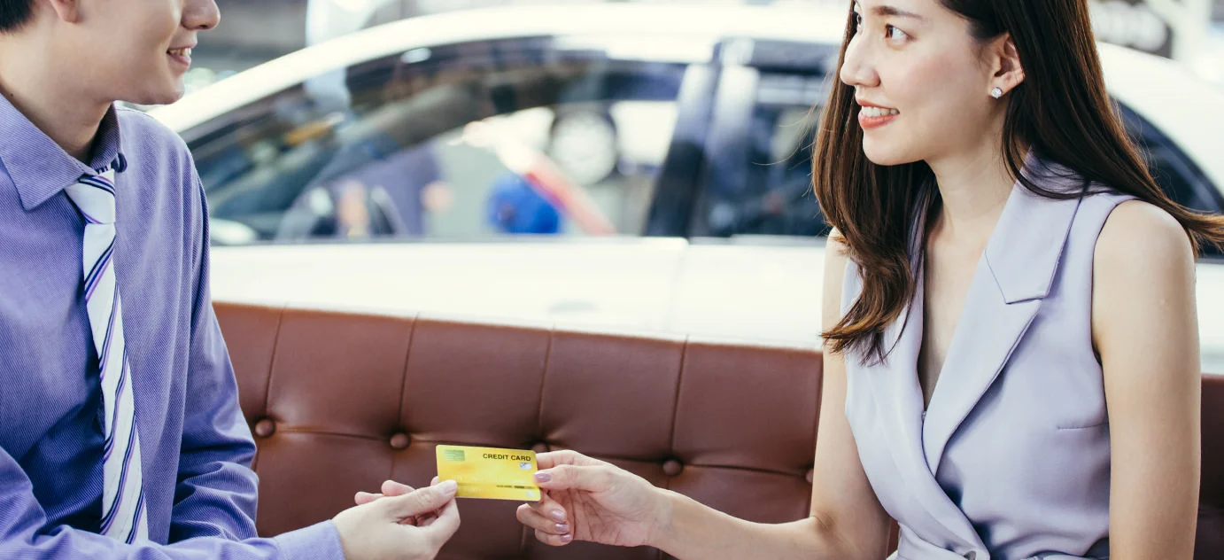 Ausschnitt eines Autos mit zwei M&auml;nnern im Hintergrund beim Handschlag.