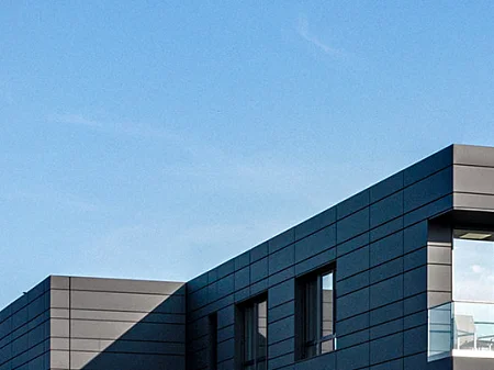 Außenansicht des DESKO Firmengebäudes mit moderner Fassade, Logo auf dem Dach und wehenden Unternehmensflaggen.