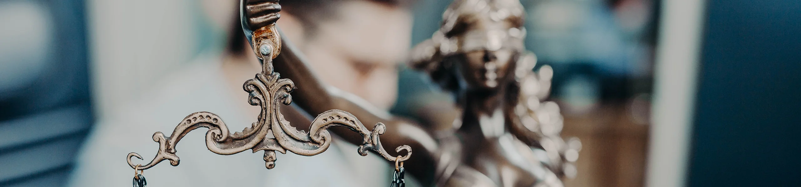 Detailaufnahme einer kunstvoll verzierten Waage mit metallenen Ornamenten, im Hintergrund unscharf eine Justitia-Figur.