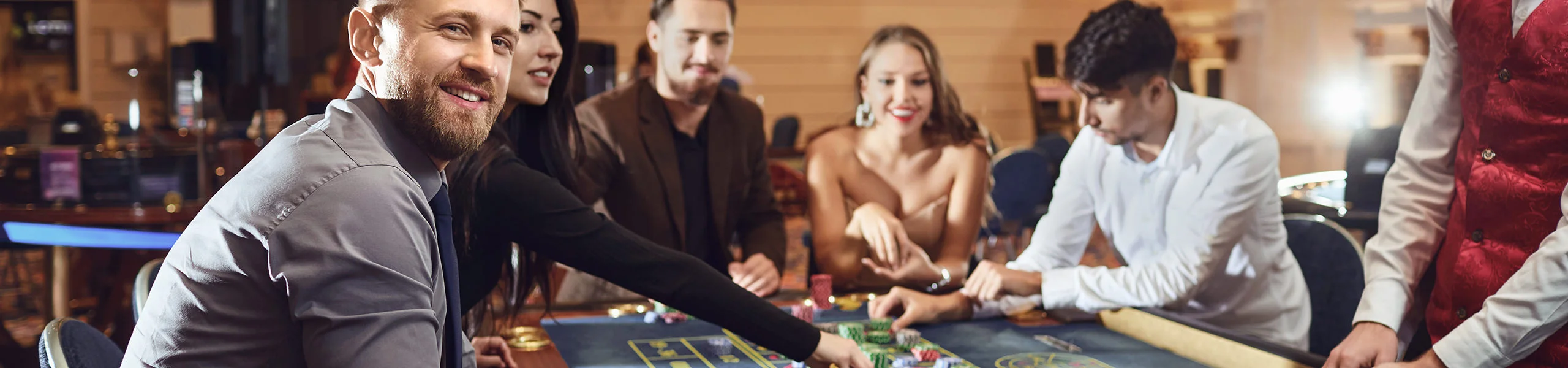 Groupe de personnes &eacute;l&eacute;gamment v&ecirc;tues assises &agrave; une table de jeu dans un casino, disposant des jetons et des cartes et jouant ensemble dans une atmosph&egrave;re conviviale.