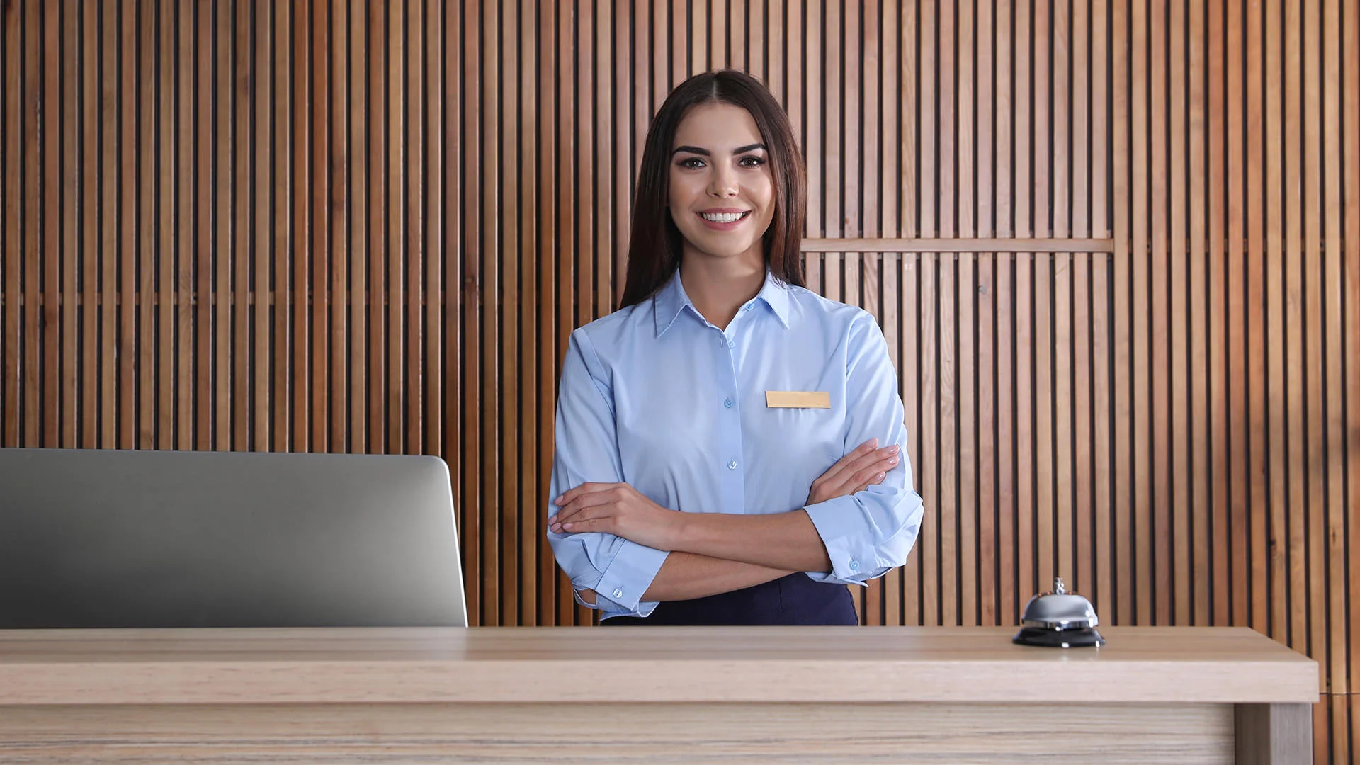 Une employ&eacute;e de l'h&ocirc;tel se tient &agrave; la r&eacute;ception, les bras crois&eacute;s devant un &eacute;cran.