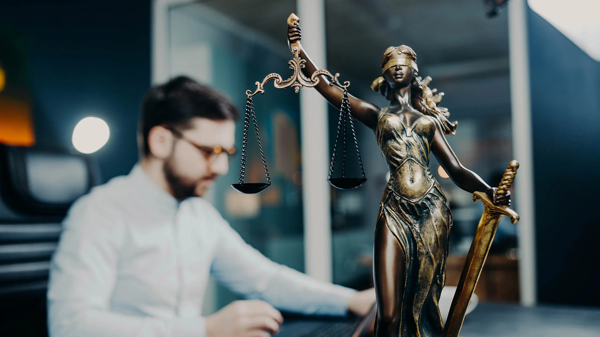 Un homme barbu est assis &agrave; un bureau dans une &eacute;tude de notaire ou un cabinet d'avocats.