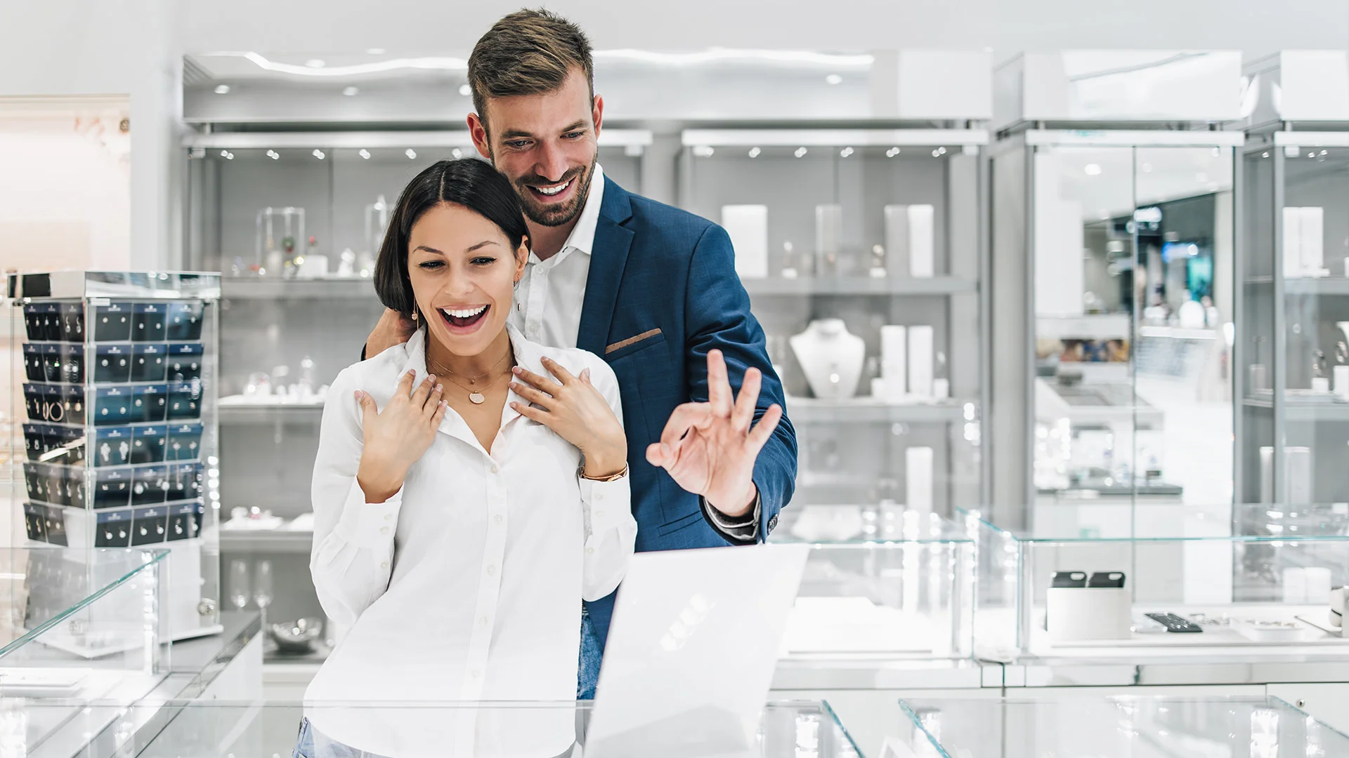 Un jeune couple souriant essaie des bijoux dans une bijouterie.