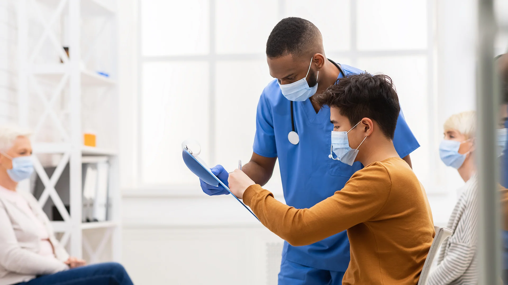 Un jeune patient portant un masque signe un document dans un &eacute;tablissement m&eacute;dical.