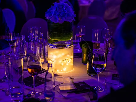 Festively laid table with illuminated glass cylinder, flower arrangement, candlelight and PENTA branding at the evening event.