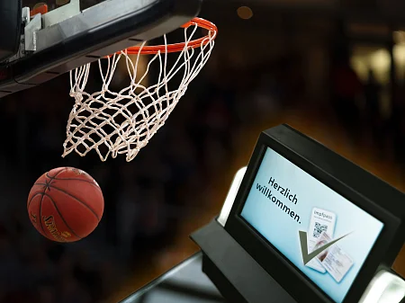 El balón de baloncesto pasa volando junto a la canasta, al lado una pantalla con un saludo y el código QR para la prueba del certificado de vacunación.