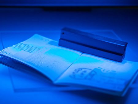 Opened passport under blue UV light scanner, security features and printed elements are visualised.