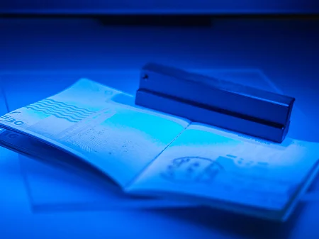 An opened passport is placed under blue UV light in a document scanner for a security check.