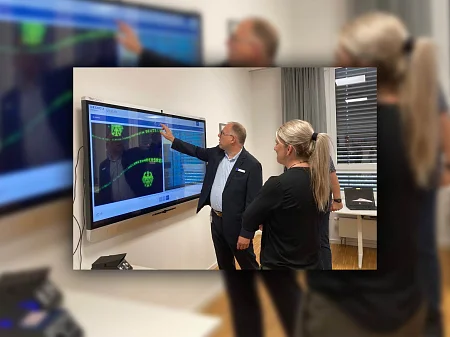 A man explains content to a woman on a large touchscreen with document verification, both are standing in an office.