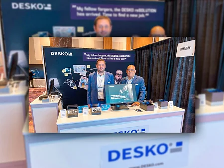 Zwei DESKO Mitarbeiter am Messestand mit reSOLUTION-Motiv, Produktpräsentation des 4X Scanners und Branding im Hintergrund.