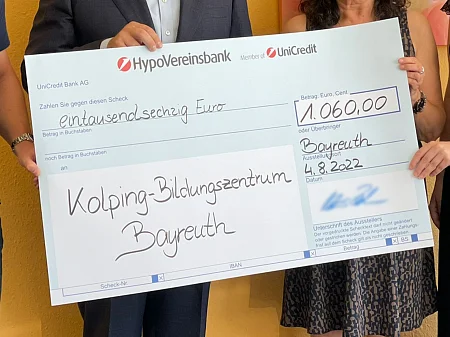 Plusieurs personnes tiennent un grand chèque de donation de 1.060 euros pour le centre de formation Kolping de Bayreuth.