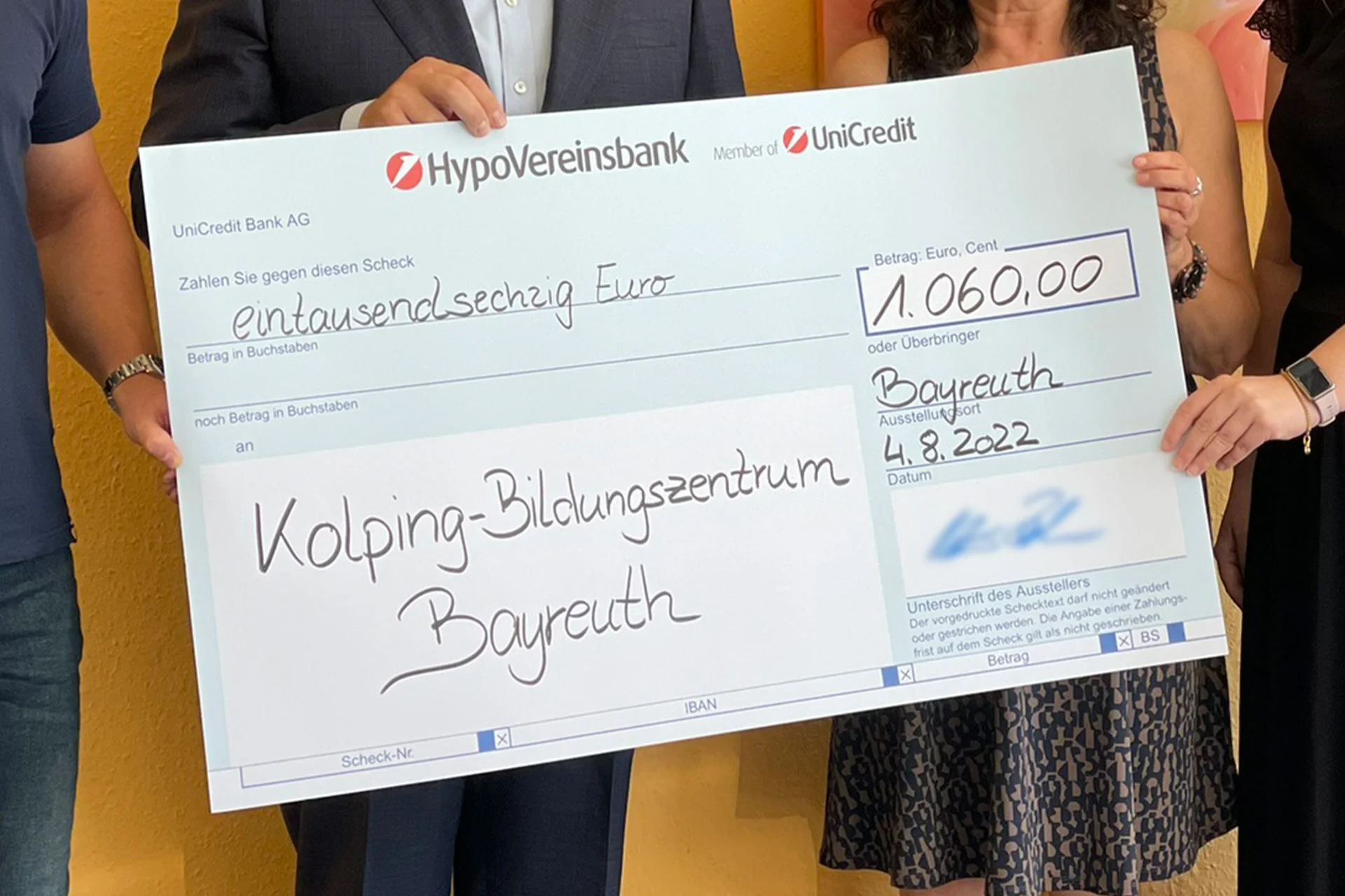 Plusieurs personnes tiennent un grand ch&egrave;que de donation de 1.060 euros pour le centre de formation Kolping de Bayreuth.
